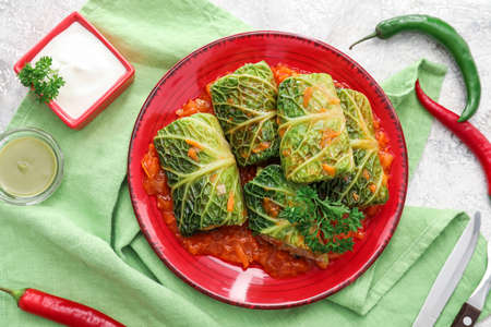 Plate with stuffed cabbage leaves, tomato sauce and ingredients on color fabric backgroundの写真素材