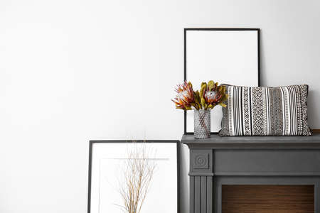 Dry flowers in vase, pillow and blank picture frames on mantelpiece near wallの写真素材