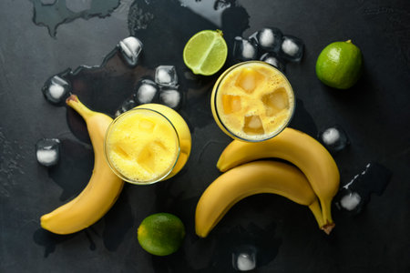 Glasses of tasty banana daiquiri cocktail, fruits and ice cubes on dark backgroundの写真素材