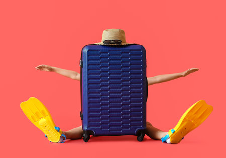 Funny little boy in paddles sitting behind suitcase on color backgroundの写真素材
