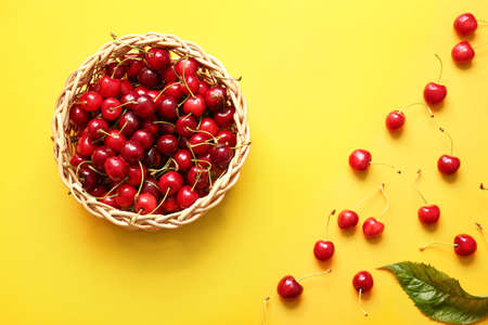 Wicker bowl with tasty ripe cherry on color background