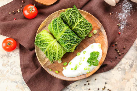 Plate with stuffed cabbage leaves and sour cream on light background