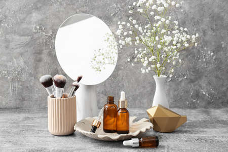 Composition with bottles of essential oil, makeup brushes, mirror and flowers on grunge backgroundの写真素材