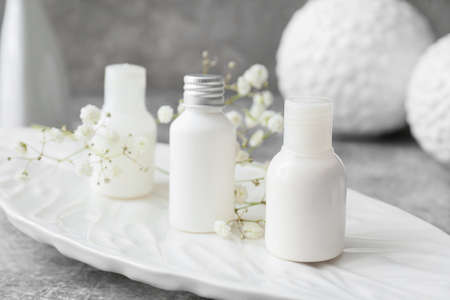 Plate with bottles of cosmetic products on table, closeup