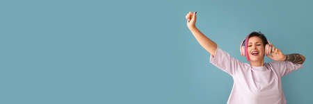 Beautiful emotional woman with dyed hair listening to music on blue background with space for textの写真素材