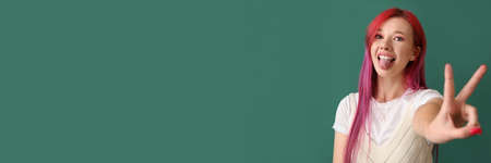Cool young woman with bright hair showing victory gesture on green background with space for text