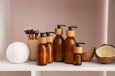 Bottles of natural cosmetic products, makeup brushes and coconut on shelf, closeupの写真素材