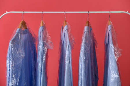 Rack with clean blue shirts in plastic bags on pink backgroundの写真素材