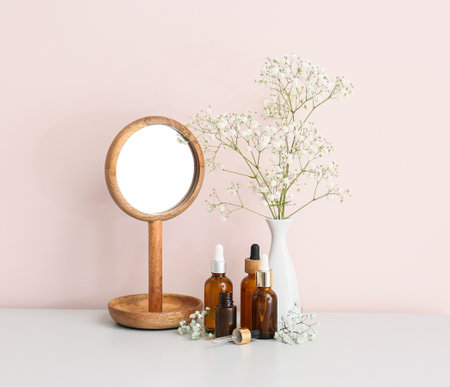 Bottles of essential oil, mirror and vase with gypsophila flowers on tableの写真素材