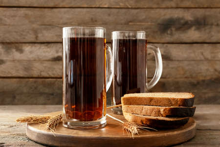 Mugs of fresh kvass and bread on wooden backgroundの写真素材
