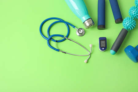 Pulse oximeter, stethoscope, bottle of water and sport equipment on color backgroundの写真素材