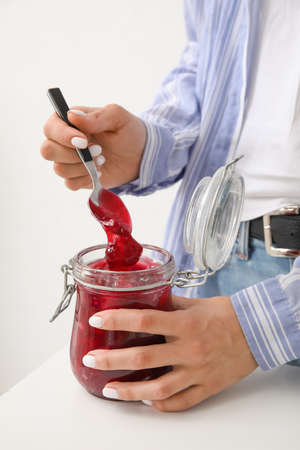 Woman with glass jar of cherry jam on light background, closeupの写真素材
