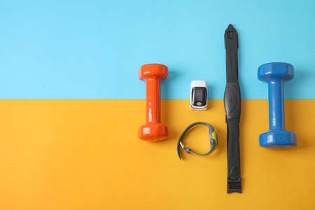 Pulse oximeter, dumbbells, fitness tracker and chest belt on color backgroundの写真素材