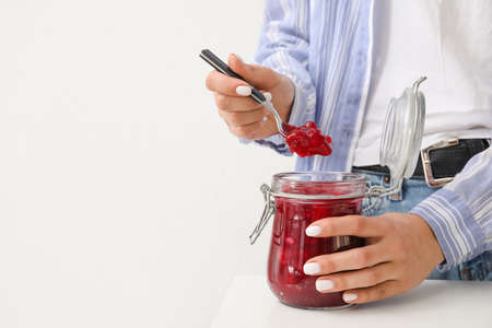 Woman with glass jar of cherry jam on light background, closeupの写真素材