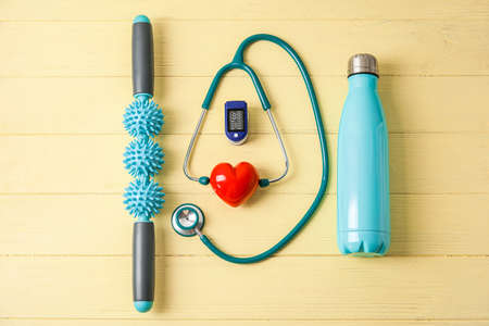 Composition with pulse oximeter, stethoscope, bottle of water, body roller and red heart on color wooden backgroundの写真素材