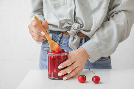 Woman with glass jar of cherry jam on light background, closeupの写真素材