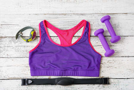 Sport top, fitness tracker, chest belt and dumbbells on light wooden backgroundの写真素材