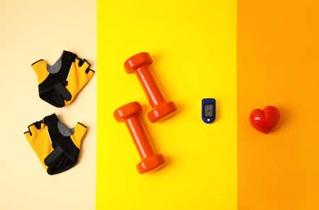 Pulse oximeter, dumbbells, bicycle gloves and heart on color backgroundの写真素材