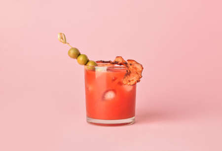 Glass of bloody mary cocktail garnished with bacon and olives on color backgroundの写真素材
