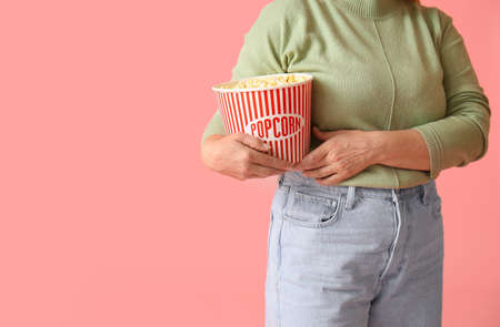 Mature woman with tasty popcorn on color backgroundの写真素材