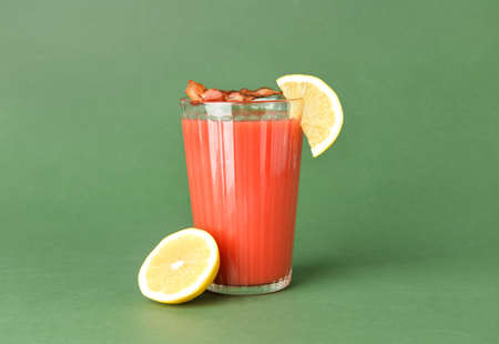 Glass of bloody mary cocktail garnished with bacon and lemon on color backgroundの写真素材