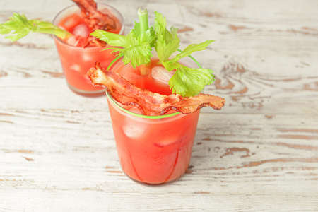 Glasses of bloody mary cocktail garnished with bacon and cilantro on light wooden backgroundの写真素材