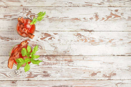 Glasses of bloody mary cocktail garnished with bacon and cilantro on light wooden backgroundの写真素材