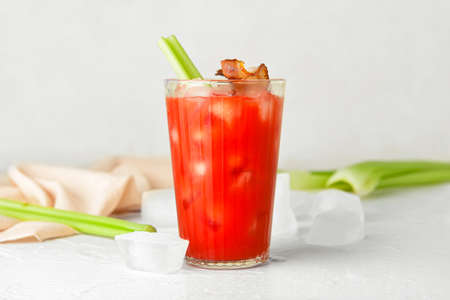 Glass of bloody mary cocktail garnished with bacon and celery on light backgroundの写真素材