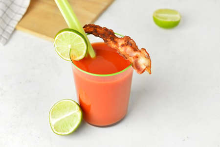 Glass of bloody mary cocktail garnished with bacon and lime on light backgroundの写真素材