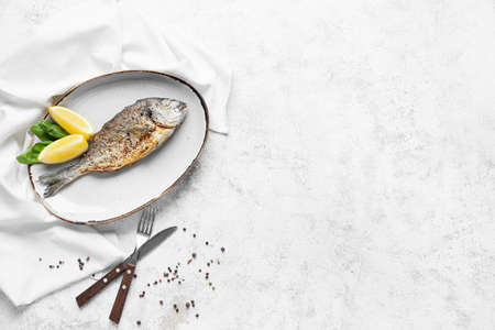 Plate with fried dorado on light background