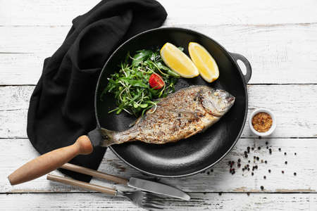Frying pan with fried dorado and salad on white wooden backgroundの写真素材