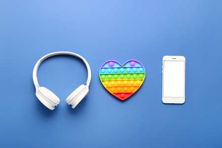 Pop it fidget toy, headphones and smartphone on color background