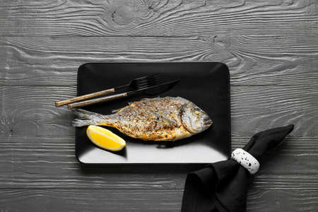 Plate with fried dorado on dark wooden background