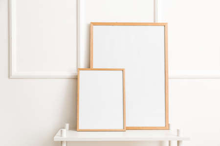 White table with blank poster frames near stylish light wall
