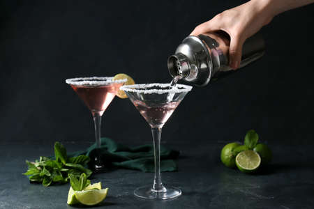 Woman pouring cocktail from shaker into glass on dark backgroundの写真素材