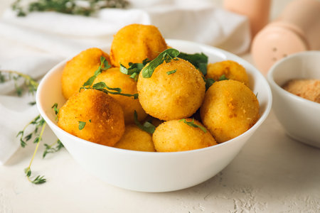 Bowl with fried potato balls on light background