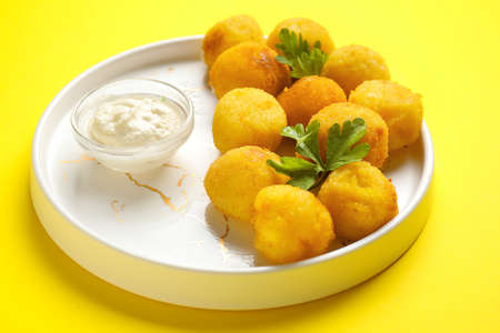 Plate with fried potato balls and sauce on color background