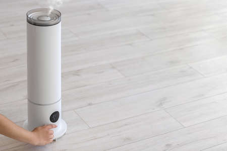 Woman switching on modern humidifier in room