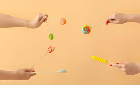 Women holding different sweet lollipops on beige background