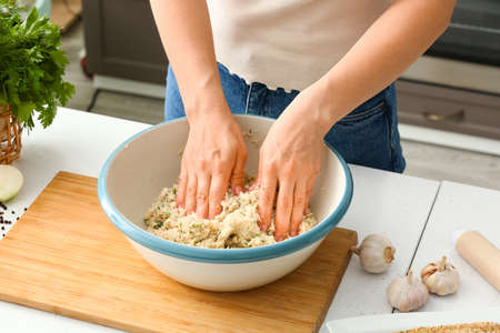 Woman cooking cod cutlets at table in kitchen