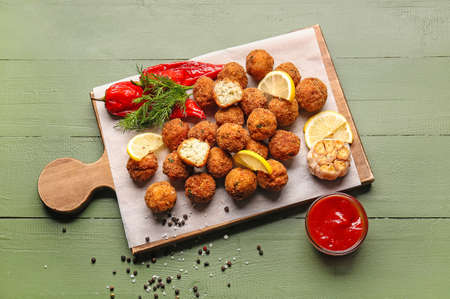 Board with tasty cod cutlets and sauce on color wooden background
