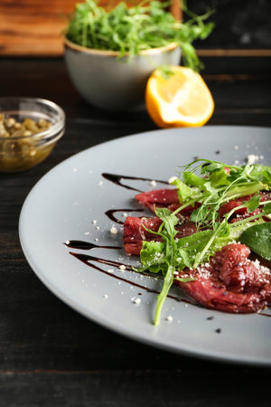 Plate with tasty veal carpaccio and ingredients on dark wooden backgroundの写真素材