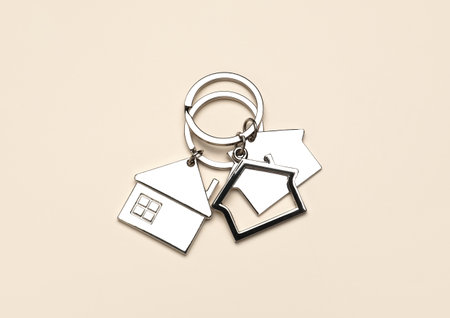 Silver house shaped keychains with keyrings on beige backgroundの写真素材