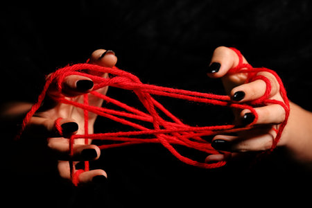 Witch hands with red rope on black backgroundの写真素材