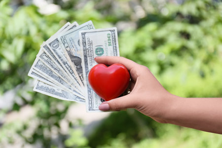 Female hand with red heart and money outdoors, closeup. Donation conceptの写真素材