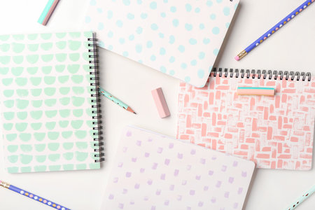 Stylish notebooks, pencils and erasers on white background, closeup