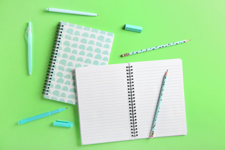 Notebooks, pens, pencils and eraser on color background