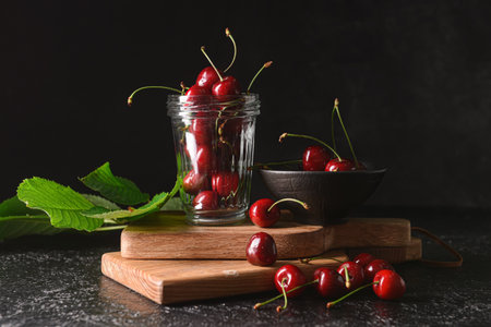 Bowl and jar with sweet cherry on dark background