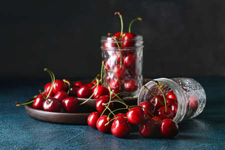 Jars with sweet cherry on dark background