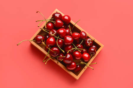 Wooden box with sweet cherry on color backgroundの写真素材